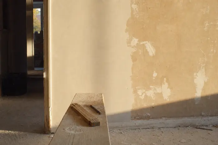 Mur en cours d'enduit, règle de maçon et planche de chêne posées au sol